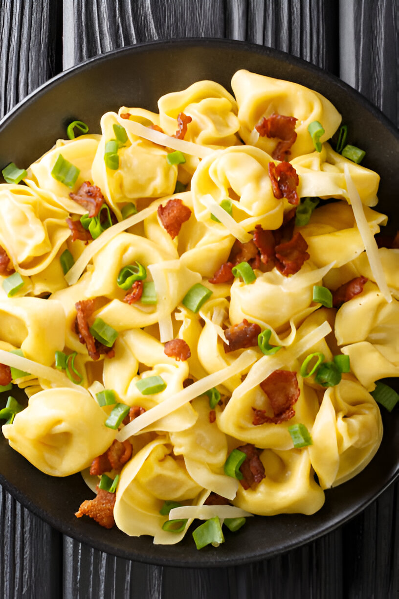 A bowl of cooked tortellini pasta topped with crispy bacon bits and chopped green onions.