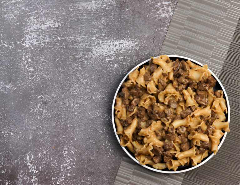 A bowl of pasta with beef chunks on a textured gray surface.