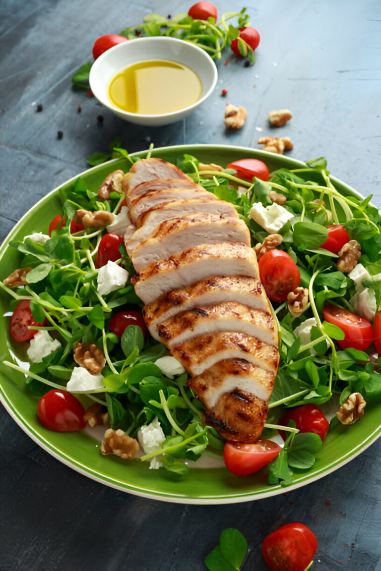 A vibrant salad with grilled chicken, cherry tomatoes, walnuts, and feta cheese served on a green plate.