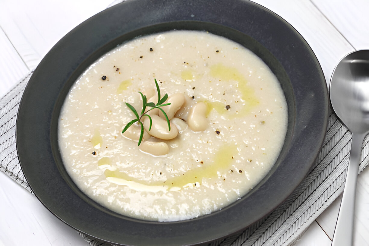 A creamy white bean soup garnished with herbs in a black bowl.