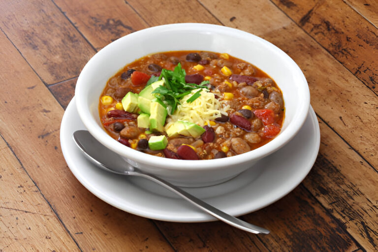 A bowl of chili topped with avocado, cheese, and cilantro on a wooden table