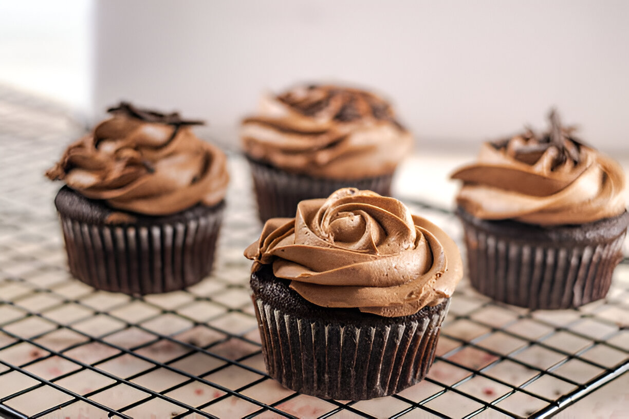 A close-up of chocolate cupcakes with creamy chocolate frosting on a cooling rack.