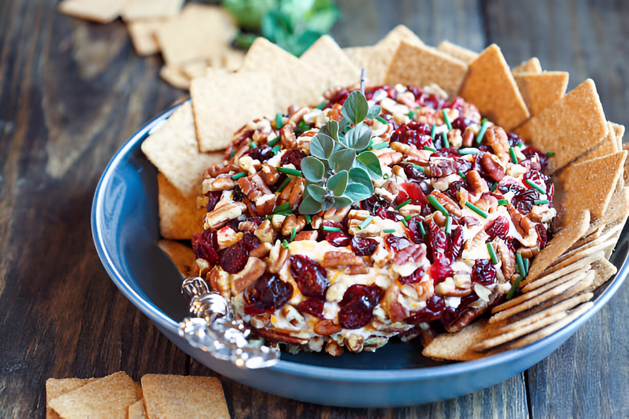 A colorful cheese ball surrounded by crackers on a wooden table.