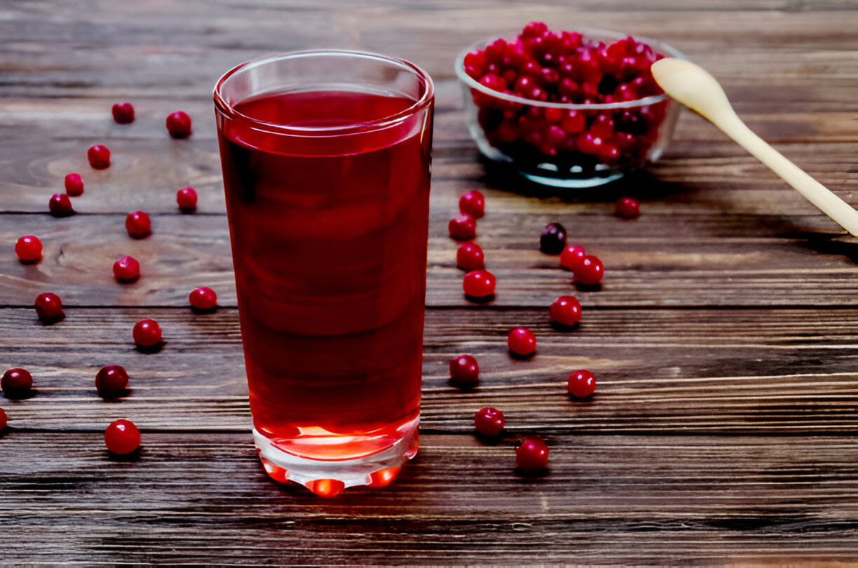 A glass of red beverage surrounded by fresh berries on a wooden table.