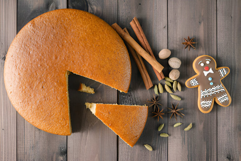 A round cake with a slice cut out, surrounded by spices and a gingerbread cookie on a wooden table.