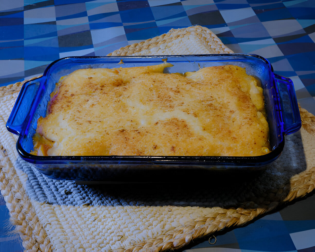A baked dish with a golden crust in a blue glass baking dish, placed on a woven mat.