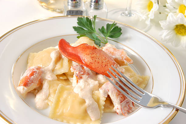 A plate of lobster ravioli topped with a piece of lobster in creamy sauce, garnished with parsley.