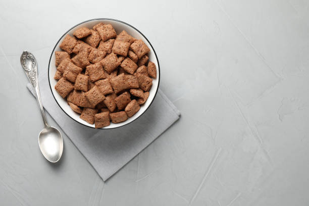 A bowl of chocolate cereal on a gray surface with a spoon beside it.