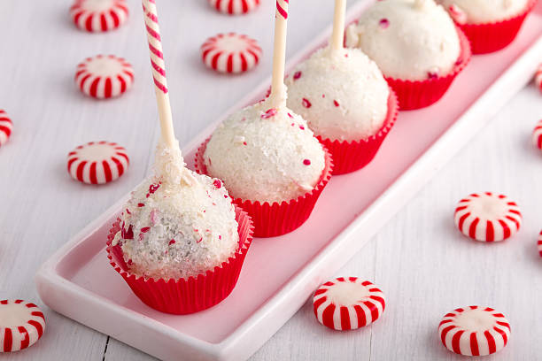 A platter of festive white cake pops topped with coconut flakes and colorful sprinkles, surrounded by peppermint candies.