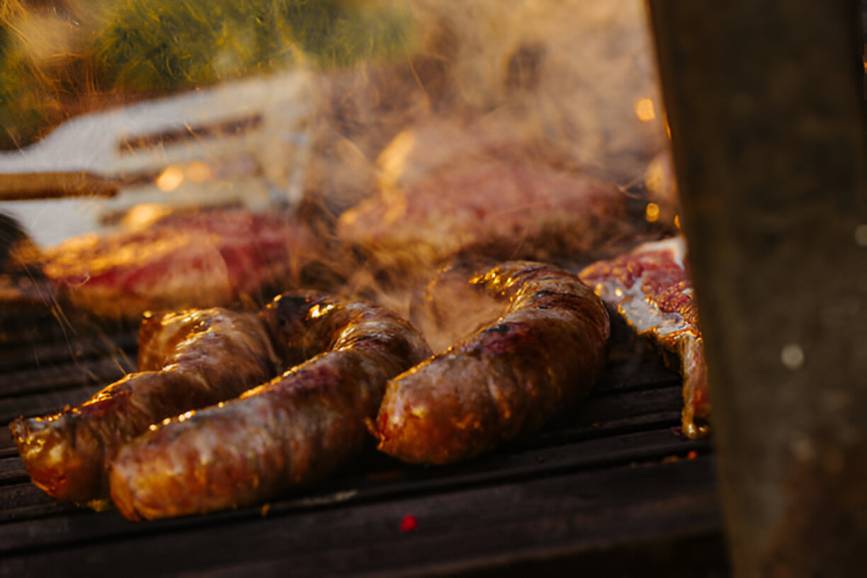 A whole cooked piece of meat resting on a wooden cutting board next to a knife and a meat fork.