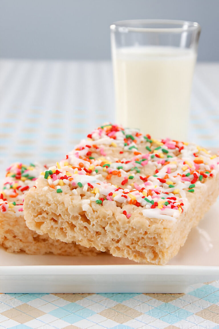 Two colorful Rice Krispie treats topped with white icing and colorful sprinkles, served with a glass of milk.