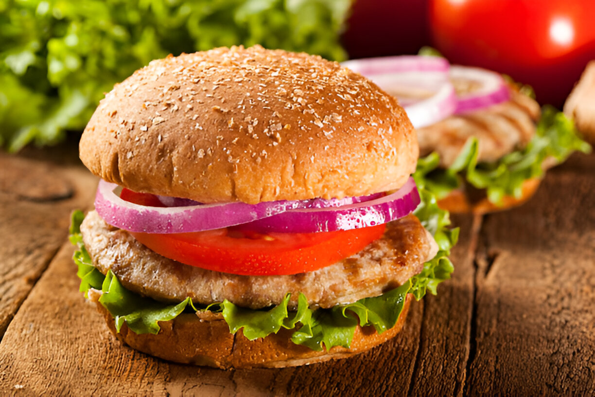 A close-up view of a delicious burger with a whole grain bun, featuring lettuce, tomato, red onion, and a meat patty, sitting on a wooden surface.
