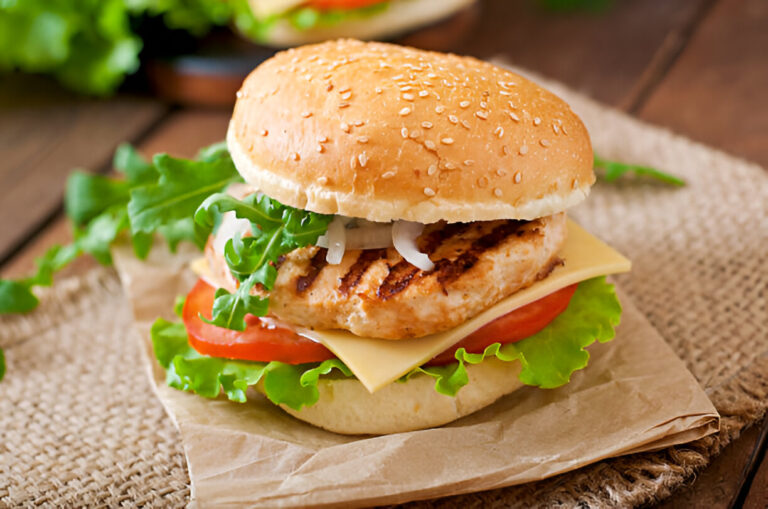 A delicious grilled chicken burger topped with lettuce, tomato, cheese, and onions, served in a sesame seed bun.