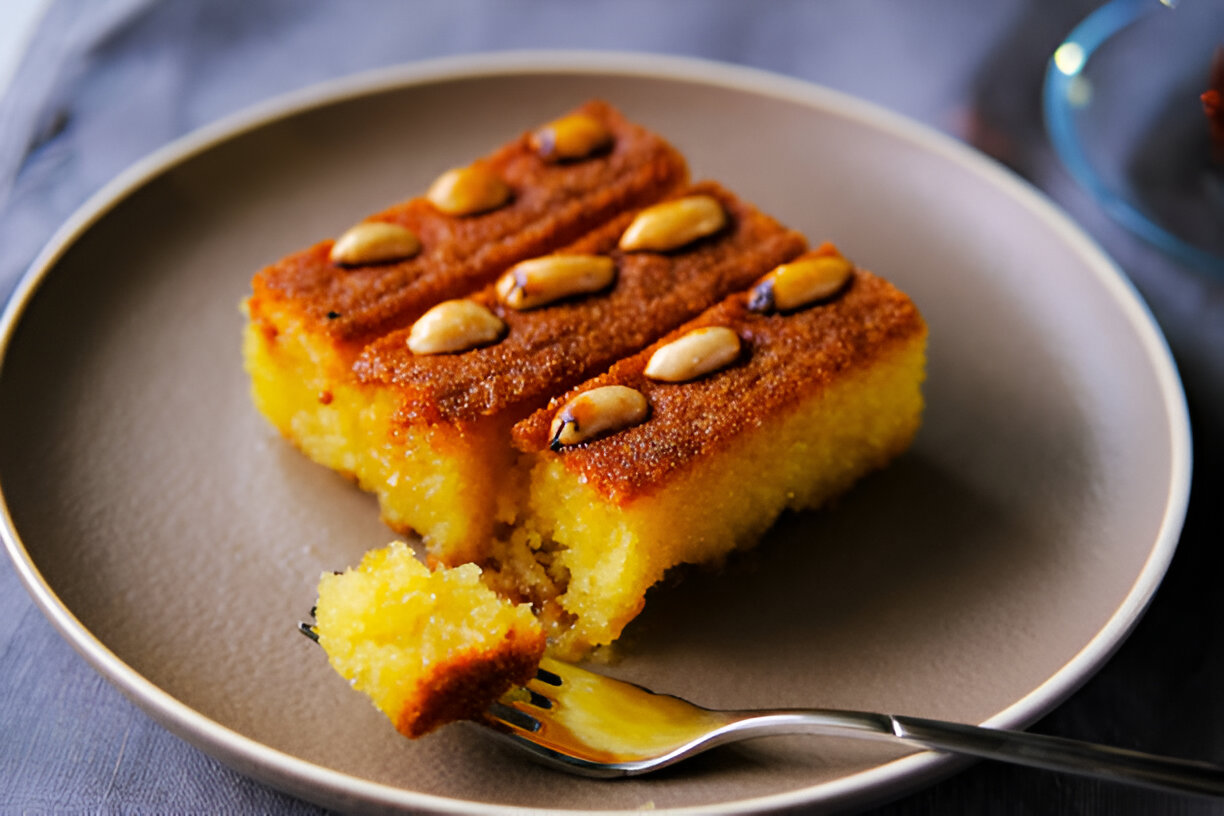 A slice of moist yellow cake topped with nuts on a round plate, with a fork beside it and a piece missing.