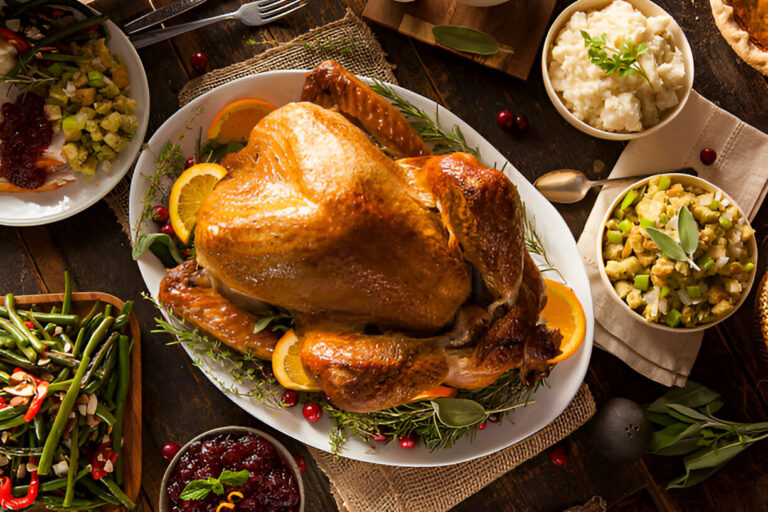 A beautifully roasted turkey garnished with orange slices and herbs, surrounded by various side dishes including stuffing and green beans on a rustic wooden table.