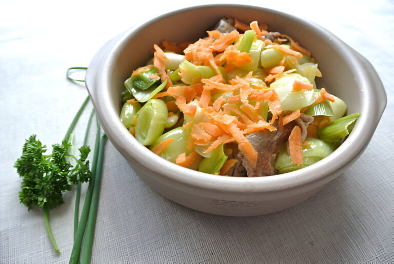 A bowl of mixed vegetables with shredded carrots and pieces of meat, garnished with green onions and parsley.