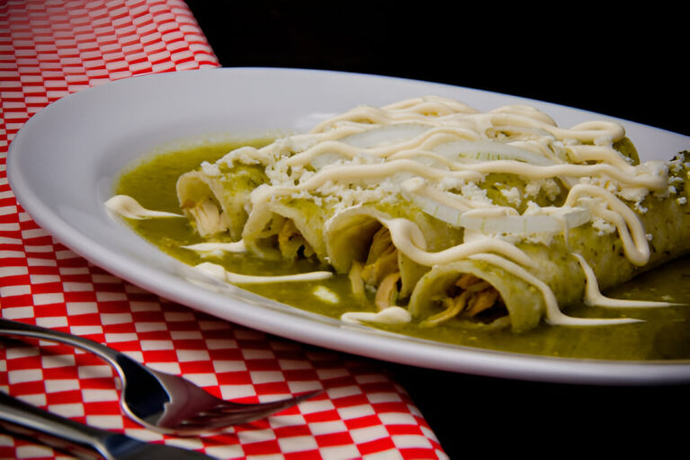 A plate of green enchiladas topped with sour cream and cheese on a red checkered tablecloth.