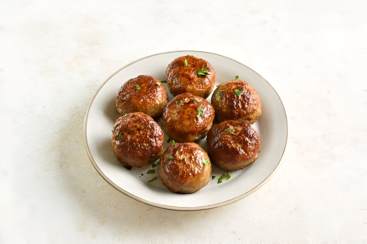A plate of golden brown meatballs garnished with green herbs.