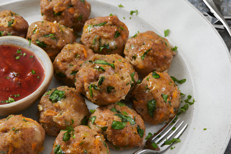 A serving of meatballs garnished with fresh herbs, accompanied by a small bowl of red sauce.