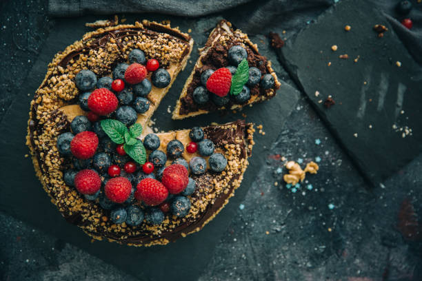 Slice of chocolate cake topped with berries and a mint leaf on a dark surface