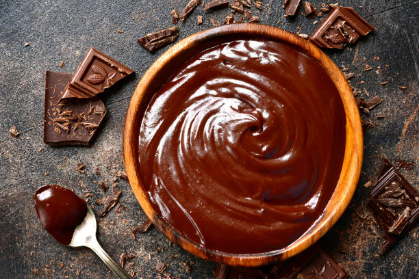Rich chocolate ganache in a wooden bowl surrounded by chocolate pieces.