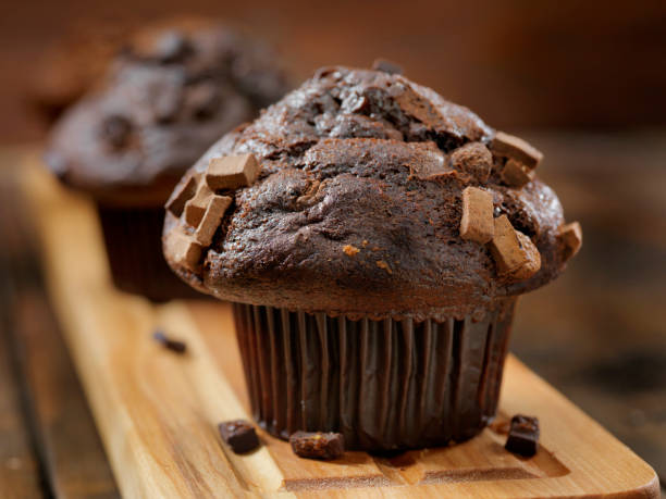 Close-up of a chocolate muffin topped with chocolate chunks, resting on a wooden serving board