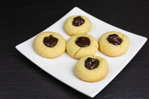 A plate of five round cookies with chocolate topping on a black background.