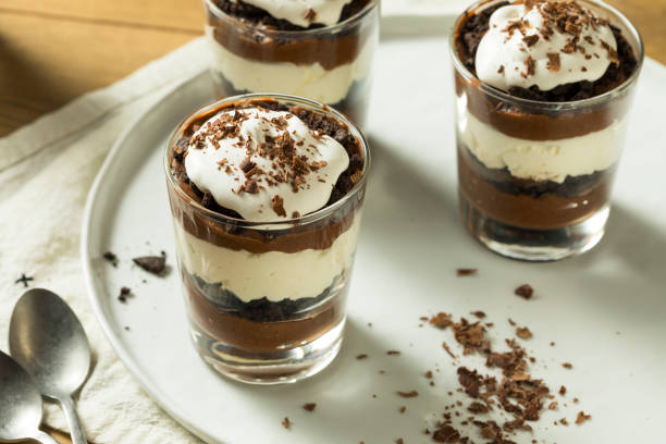 Delicious chocolate parfaits in glass cups topped with whipped cream and chocolate shavings on a white plate.