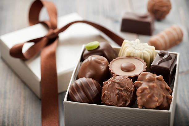 A beautifully arranged assortment of chocolates in a small gift box with a brown ribbon on a rustic wooden surface.