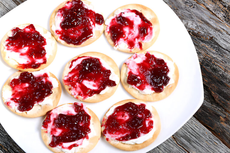 A plate of round crackers topped with cream cheese and a layer of red jelly.