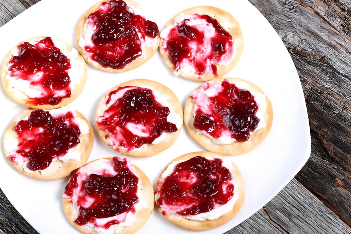 A plate of round crackers topped with cream cheese and a layer of red jelly.