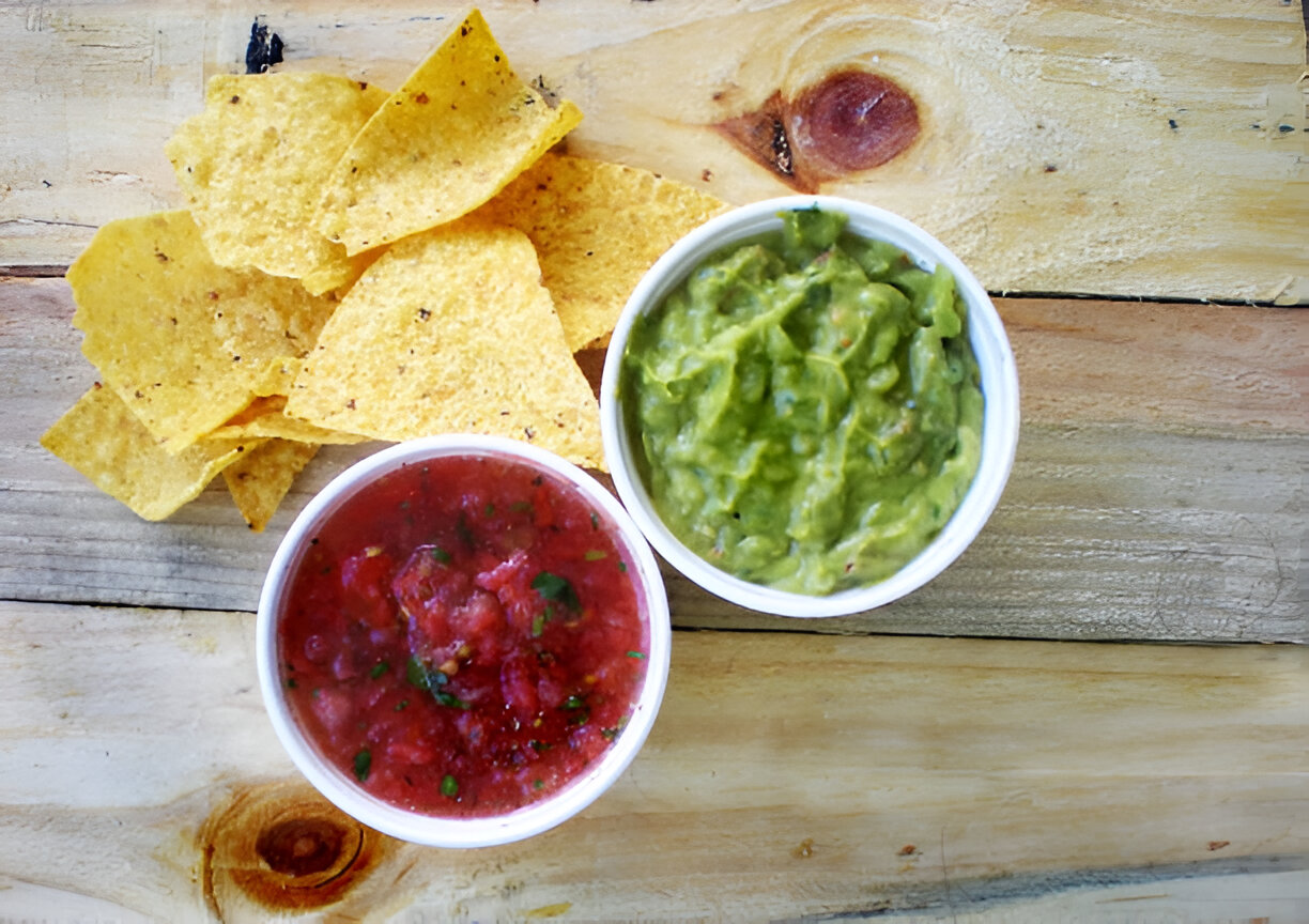 A bowl of guacamole and a bowl of salsa with tortilla chips on a wooden surface