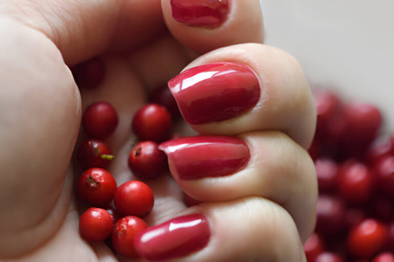 A close-up image of a hand holding red berries with manicured nails painted in a glossy red shade.