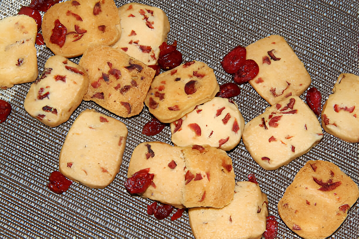 A variety of cookies with dried fruit pieces scattered on a textured surface.