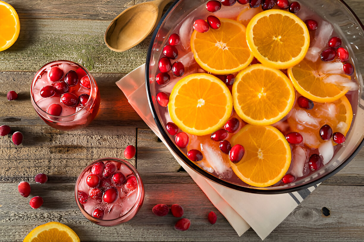 A refreshing fruit punch made with orange slices and cranberries, served in a large bowl and two glasses on a wooden table.
