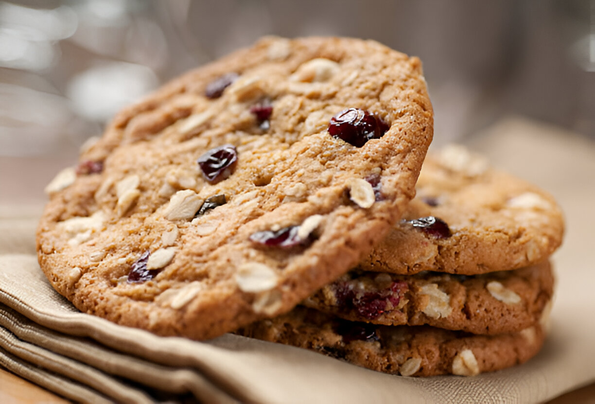 Three oatmeal cookies with cranberries stacked on a beige cloth napkin.
