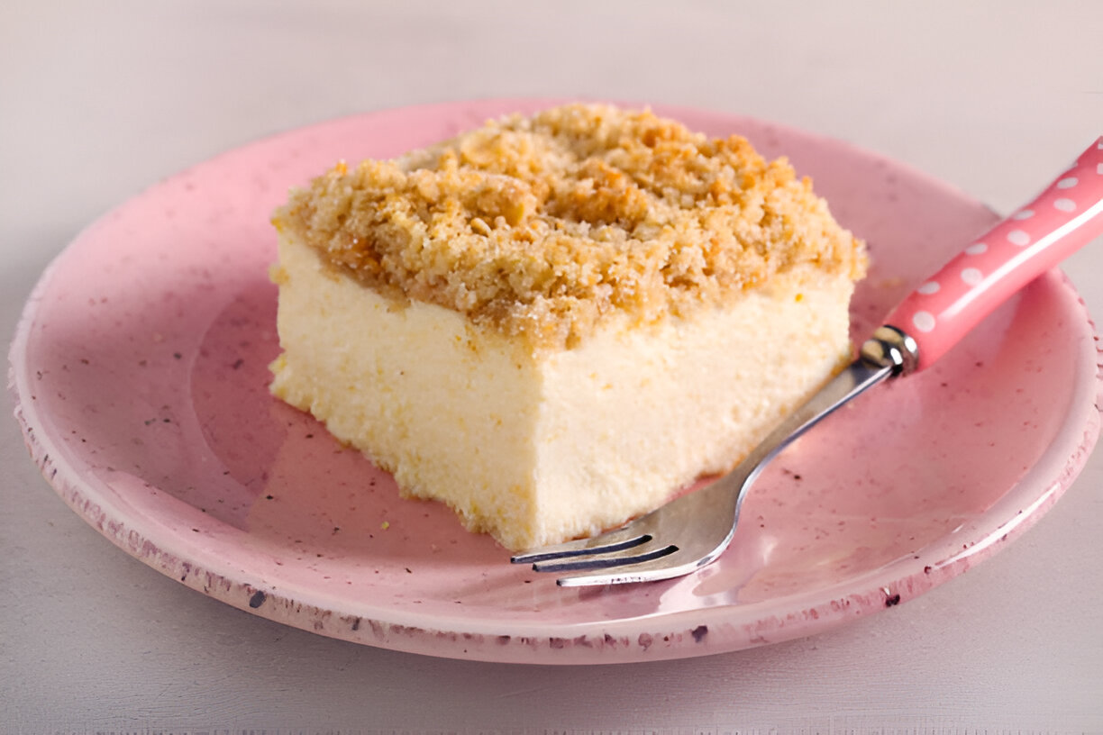 A slice of creamy dessert topped with crumbly topping on a pink plate with a fork.