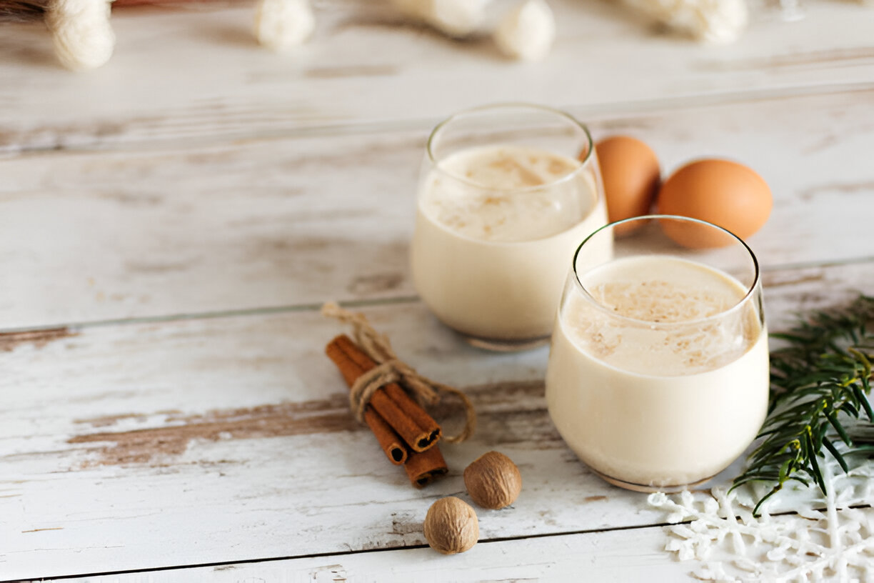 Two glasses of creamy beverage with eggs and spices on a wooden surface.