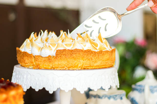 A hand using a cake server to slice a beautiful meringue-topped cake on a decorative cake stand.
