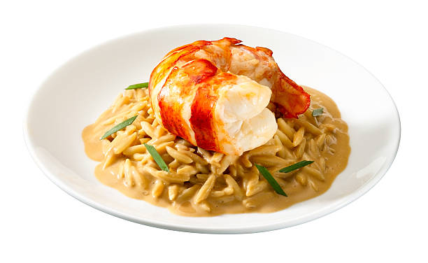 A plate of orzo pasta topped with a large lobster tail in a creamy sauce.