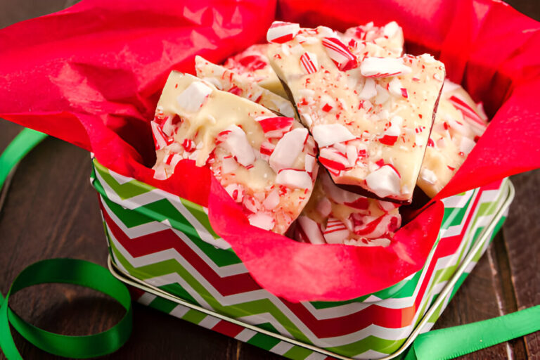 A colorful gift tin filled with peppermint bark on red tissue paper.