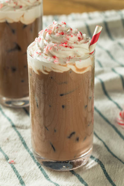 A chilled glass of peppermint mocha topped with whipped cream and crushed candy canes, placed on a striped cloth.