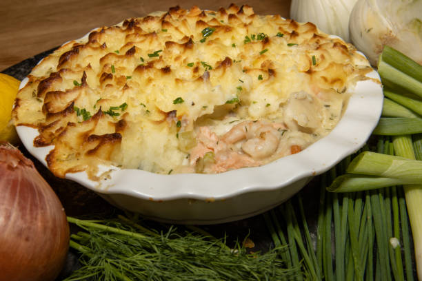 A creamy fish pie topped with golden mashed potatoes, surrounded by fresh vegetables and herbs.