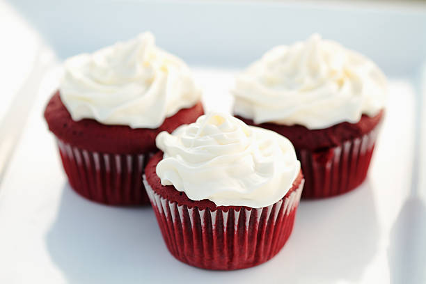 Three red velvet cupcakes topped with white cream frosting, arranged on a white platter.