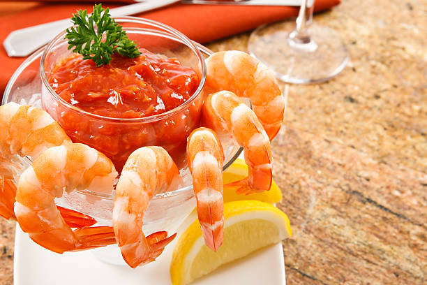 A glass bowl of shrimp cocktail garnished with parsley and lemon slices on a plate.