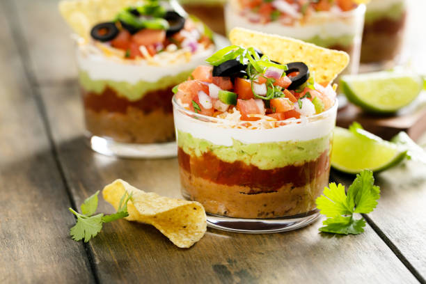 Layered dip in glass cups with tortilla chips and fresh ingredients