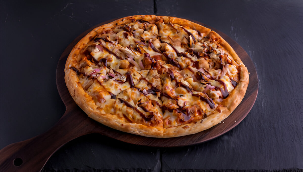 A freshly baked pizza topped with chicken and barbecue sauce on a wooden pizza board.