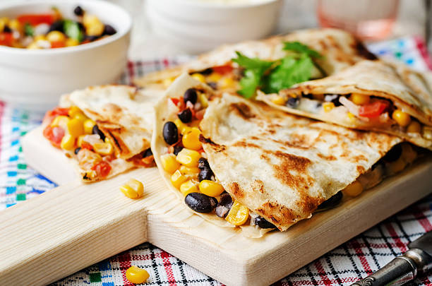 Delicious quesadillas filled with black beans, corn, and tomatoes, served on a wooden cutting board.