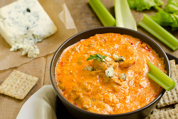 A bowl of spicy buffalo chicken dip garnished with celery sticks and blue cheese, served with crackers.