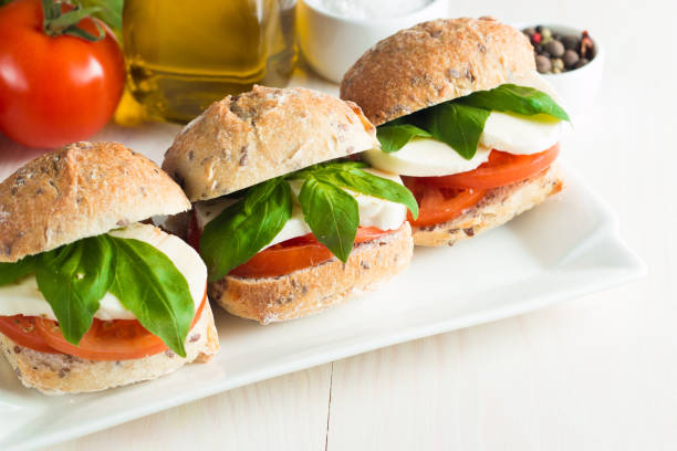 Three fresh sandwiches with basil, tomato, and mozzarella on a white plate.